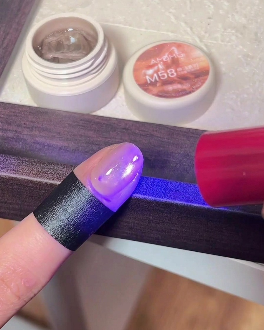 Nahaufnahme eines Fingers mit Cat-Eye-Gel-Lack unter dem violetten Licht einer UV/LED-Nagellampe.
