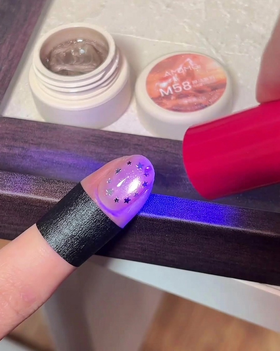 Ein Finger mit Stern-Glitzer-Design, der unter dem violetten Licht einer UV/LED-Lampe ausgehärtet wird.