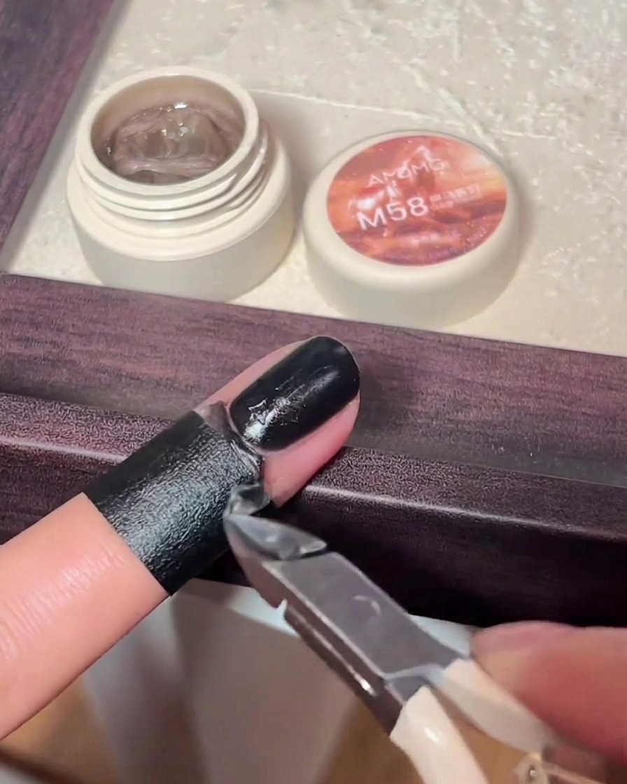 Ein kleiner Nailart-Pinsel bemalt einen erhabenen Kreuz-Charm auf einem Fingernagel mit schwarzem Gel-Lack.