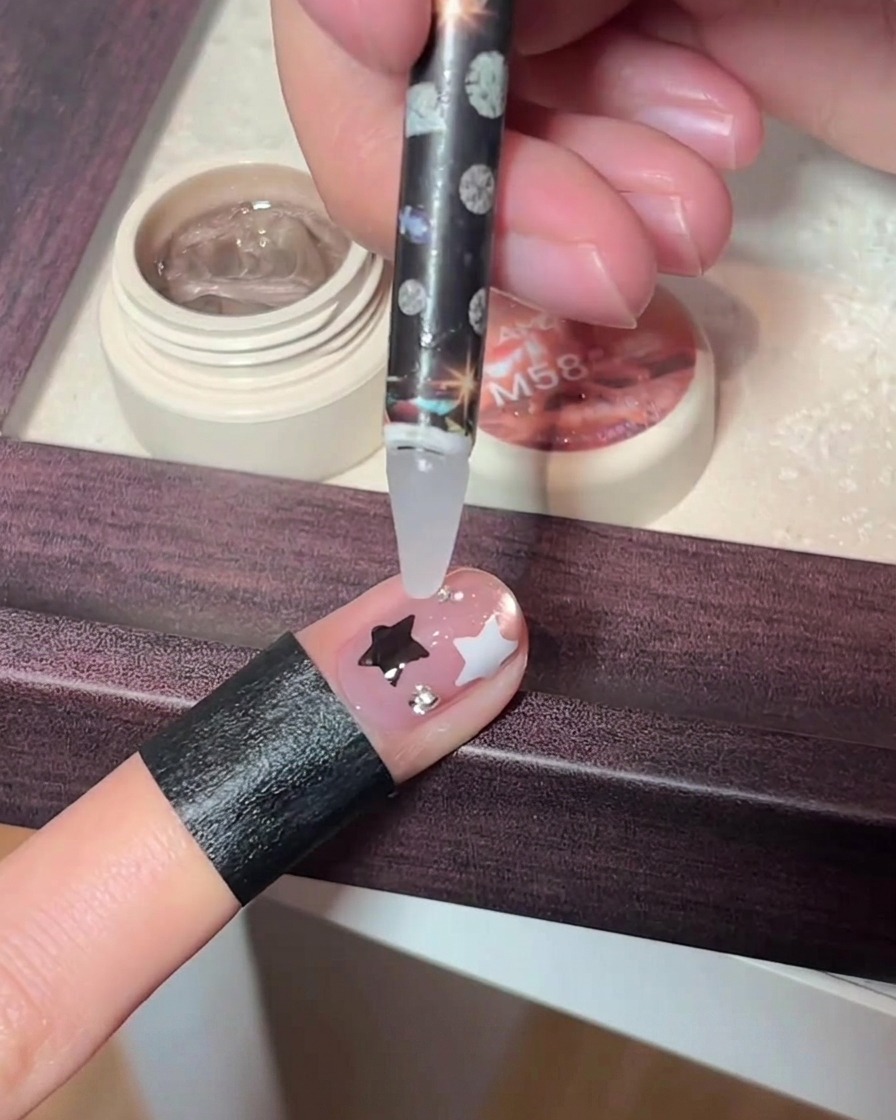 Ein Präzisionswerkzeug platziert winzige Strasssteine auf einem verzierten Fingernagel.