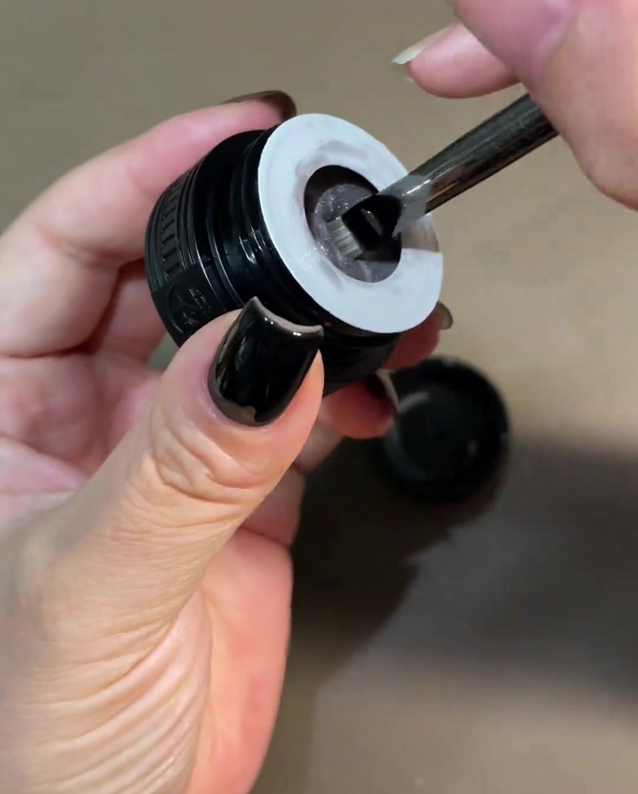 Ein kleiner Pinsel taucht in einen Tiegel mit perlmuttweißem Cat-Eye-Gel ein.