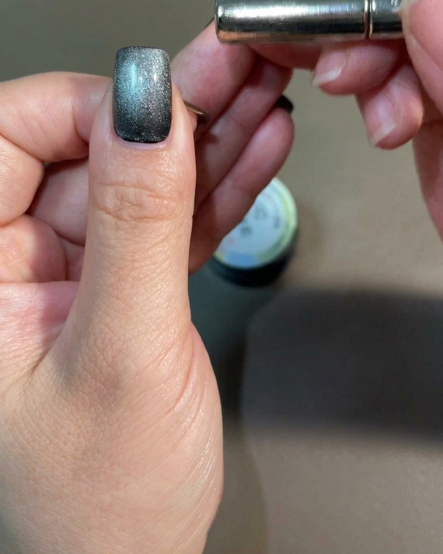 Ein Stabmagnet wird nahe an die Seite eines Fingernagels gehalten, um die Cat-Eye-Pigmente zu beeinflussen.