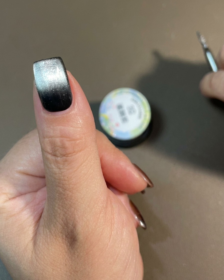 Eine Hand mit einem fertigen Cat-Eye-Farbverlauf härtet in einer Nagellampe aus.