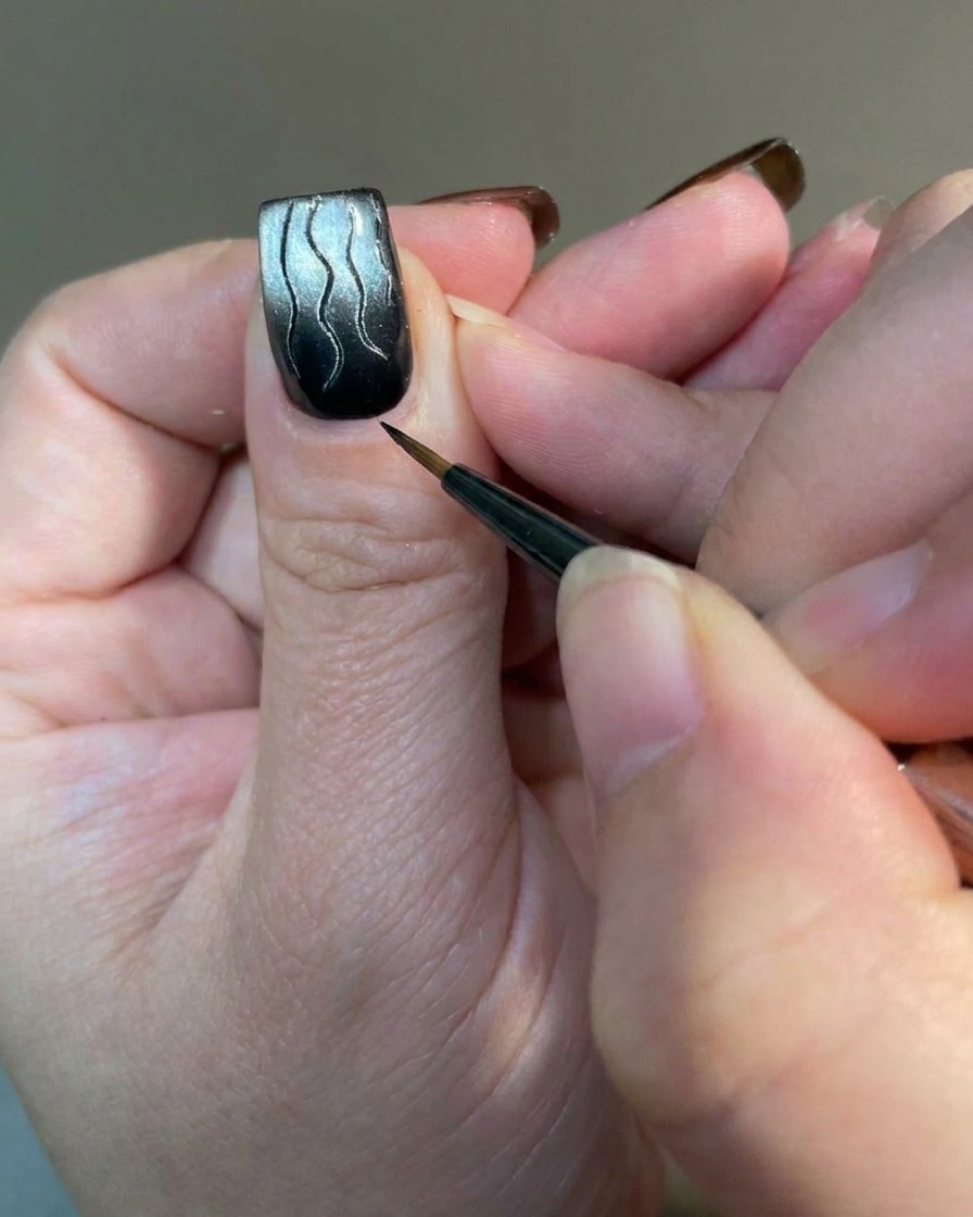 Eine Makroaufnahme eines Liner-Pinsels, der kleine, feine Akzentlinien an der Basis eines Flammen-Designs hinzufügt.