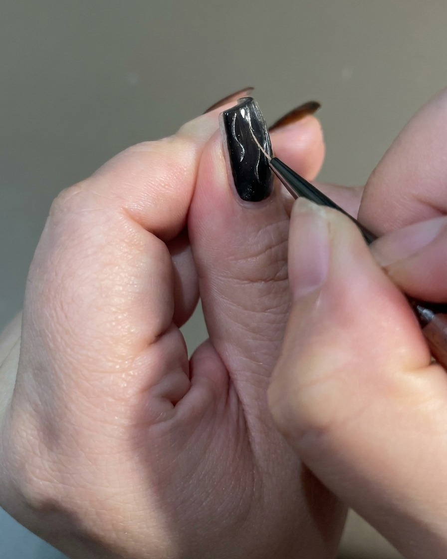 Nahaufnahme eines Liner-Pinsels, der die Enden von Flammen-Designs auf einem Nagel verjüngt, um ein scharfes, unregelmäßiges Finish zu erzielen.
