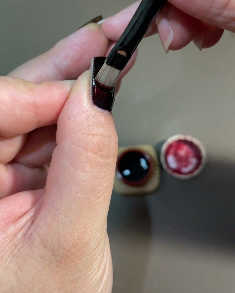 Nahaufnahme einer Hand, die in einer UV-Nagellampe platziert ist, um die frisch aufgetragene rote Gel-Schicht auszuhärten.