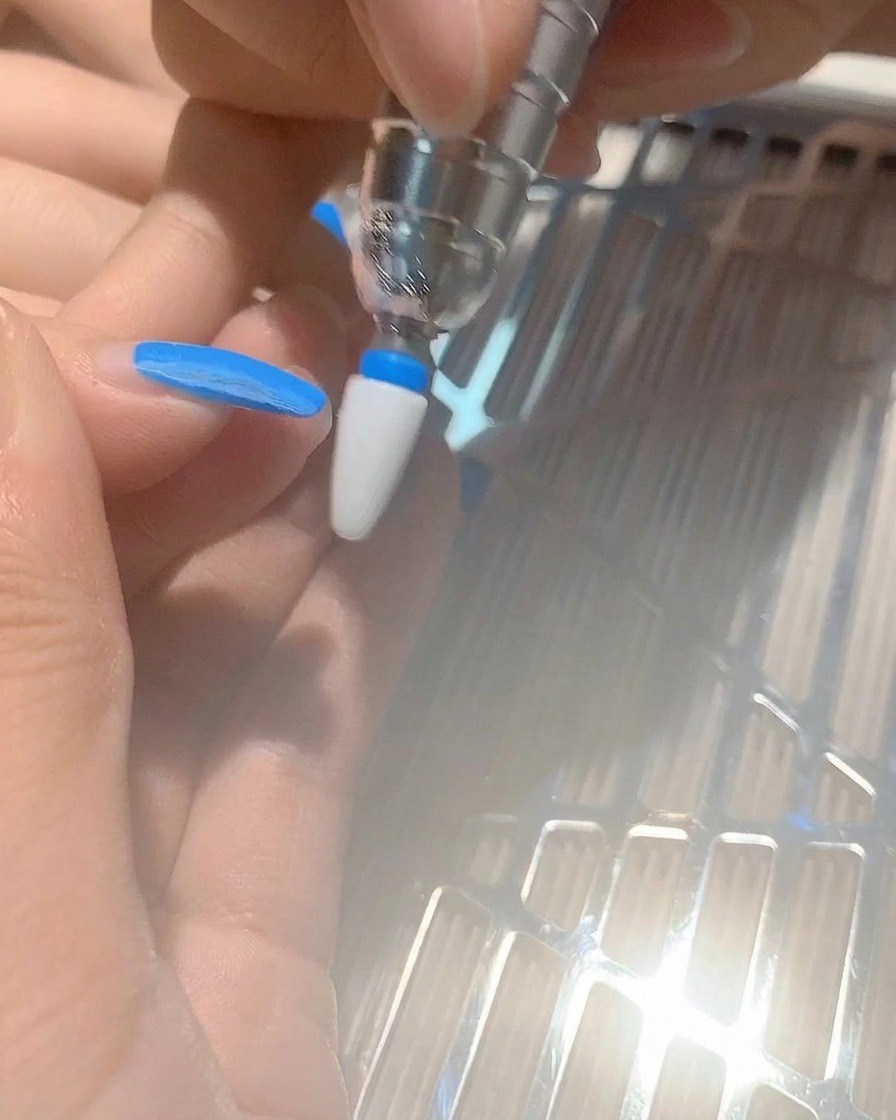 Eine Nahaufnahme eines Nagelfräser-Aufsatzes, der blaues Gel von einem Fingernagel entfernt.