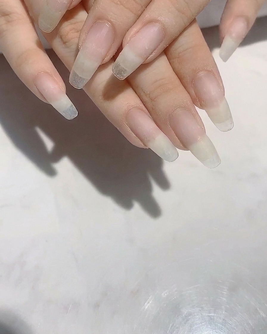 Hände mit langen, geformten Naturnägeln, die mit einer Nagelfeile in Form gebracht werden.
