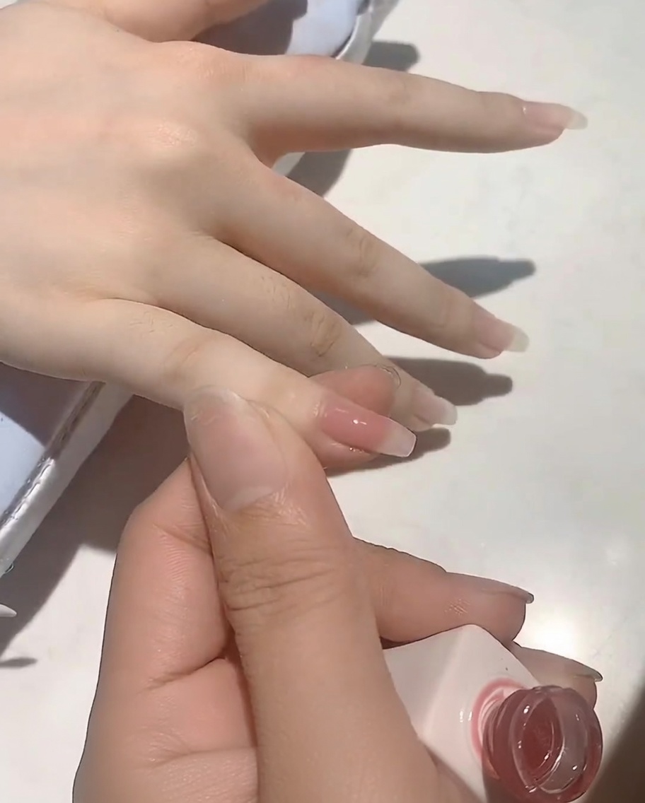 Ein Pinsel, der ein sanftes Nude-Rosa Gel auf einen Naturnagel aufträgt.