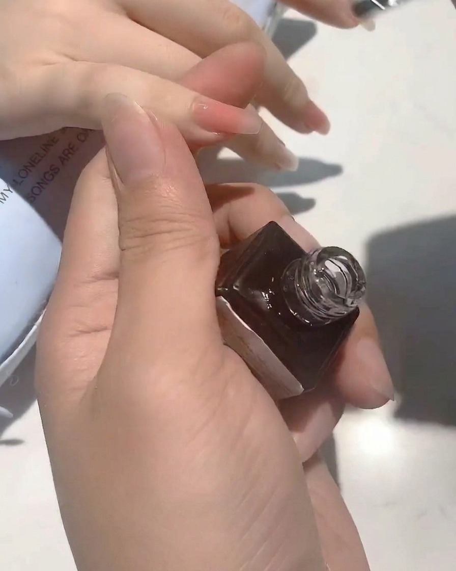 Eine Nahaufnahme eines Pinsels, der einen klaren, glänzenden Top Coat auf einen nudefarbenen Nagel aufträgt.