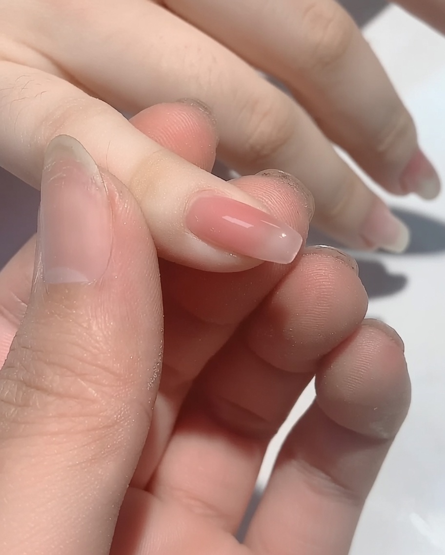 Nahaufnahme eines Applikators, der irisierendes Puder auf den Spitzenbereich eines polierten Nagels aufträgt.