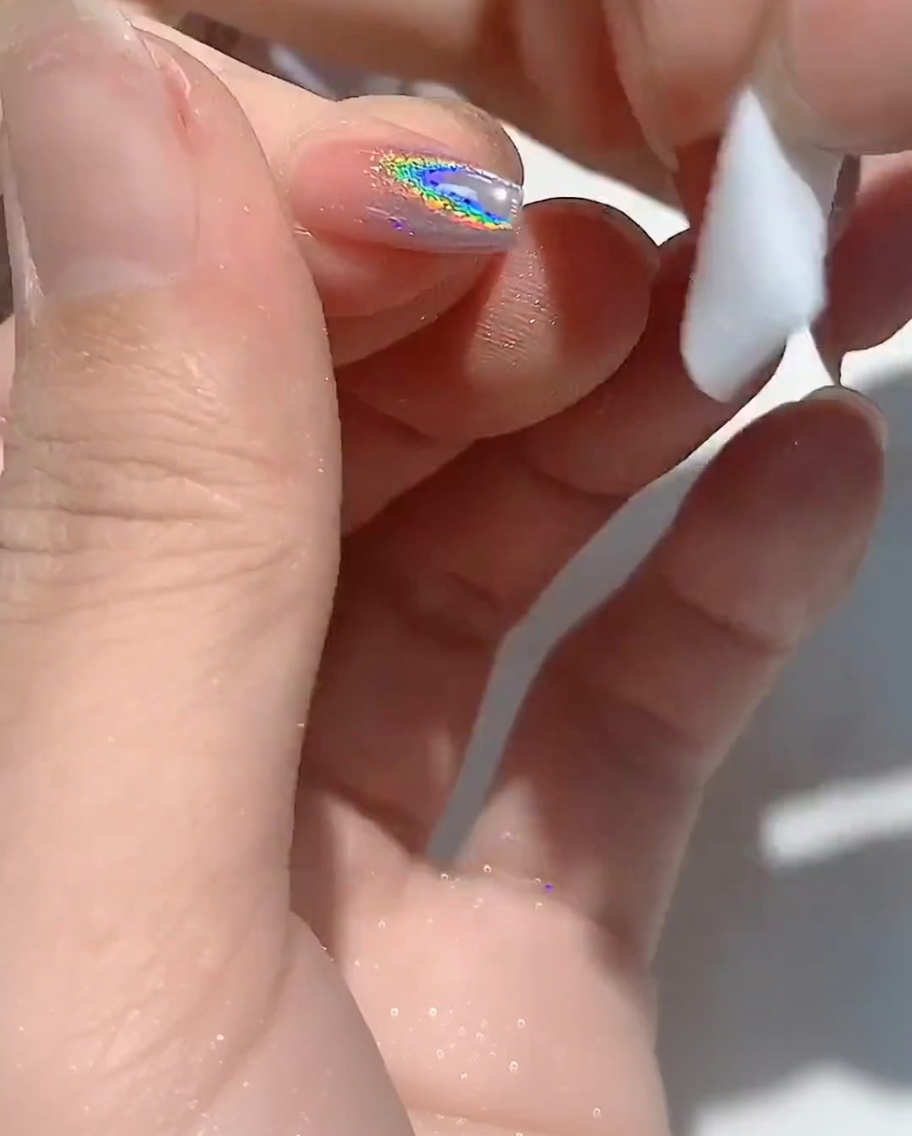 Ein fusselfreies Tuch reinigt den Rand eines Fingernagels.
