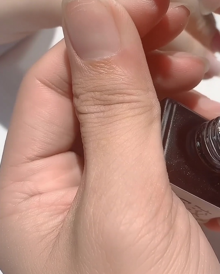 Ein Pinsel trägt eine klare, viskose Rubber Base über einen Nagel mit irisierenden Details auf.