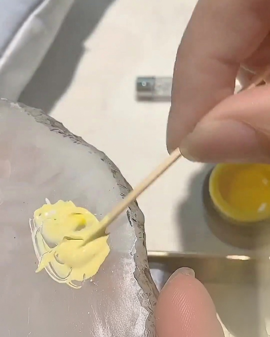 Ein kleiner Punkt rotes Gel wird zur bestehenden gelben Mischung auf einer Palette hinzugefügt.