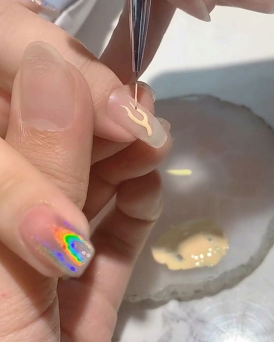 Ein Nageldesigner nutzt einen feinen Liner-Pinsel, um eine zarte Flammen-Kontur auf eine Nagelspitze zu malen.