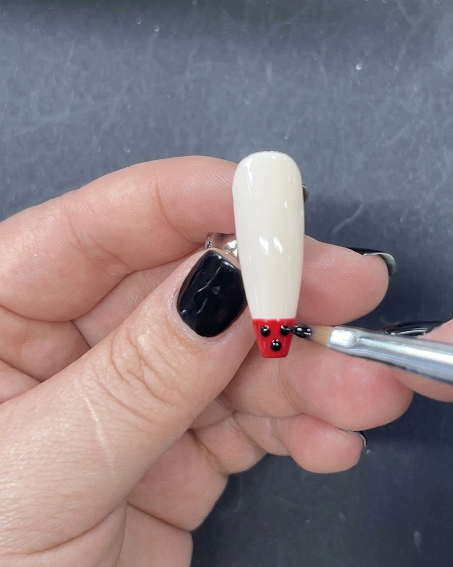 Ein feiner Liner-Pinsel trägt einen horizontalen Streifen rotes Gel direkt über der schwarzen Spitze auf.