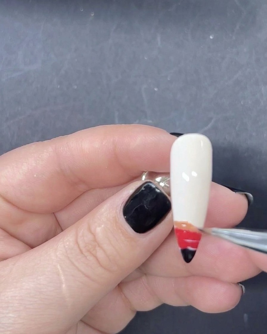 Ein feiner Liner-Pinsel fügt dem Farbverlauf auf dem Nagel einen orangenen Streifen hinzu.