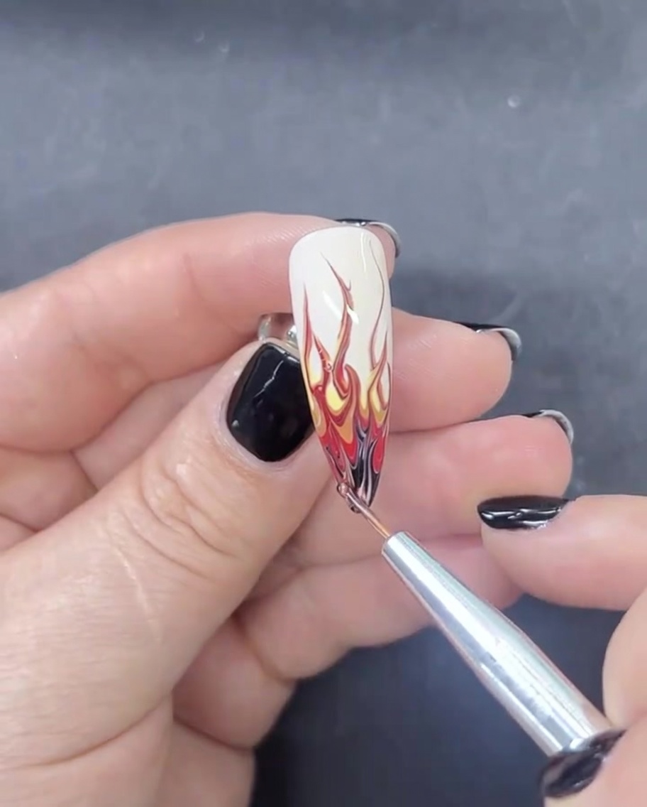 Ein feiner Liner-Pinsel trägt eine winzige Menge schwarzes Gel auf die Spitze eines mandelförmigen Nagels auf, um das Design abzuschließen.