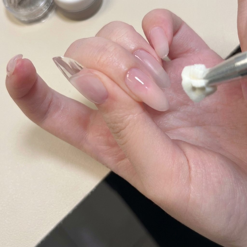 Ein Metallwerkzeug trägt weißes festes Gel auf die Nagelspitze auf und drückt es flach.