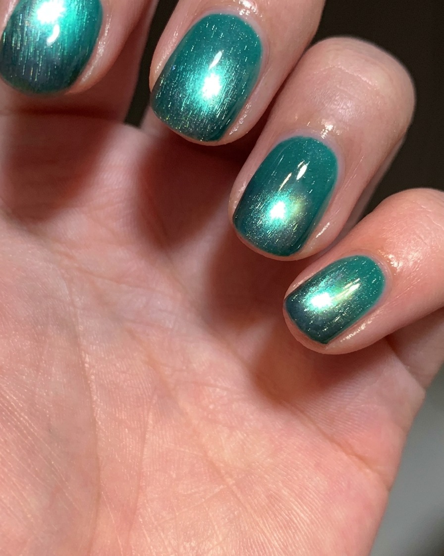 Ein Pinsel trägt eine Schicht leuchtend seegrünes Cat-Eye-Gel auf einen Nagel mit schwarzer Spitze auf.