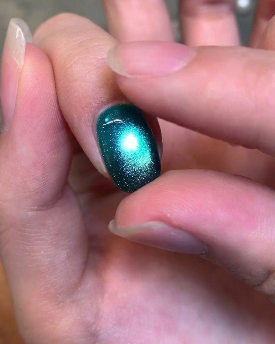 Nahaufnahme eines Fingers, der sanft die Textur eines fertigen, glänzenden tiefgrünen Cat-Eye-Gelnagels testet.