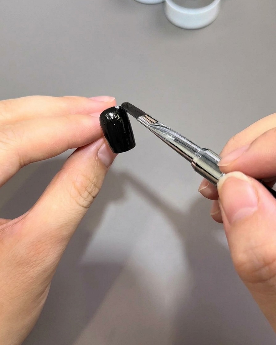 Ein Nagelpinsel trägt eine gleichmäßige Schicht schwarzen Gellacks auf eine vorbereitete Nageloberfläche auf.