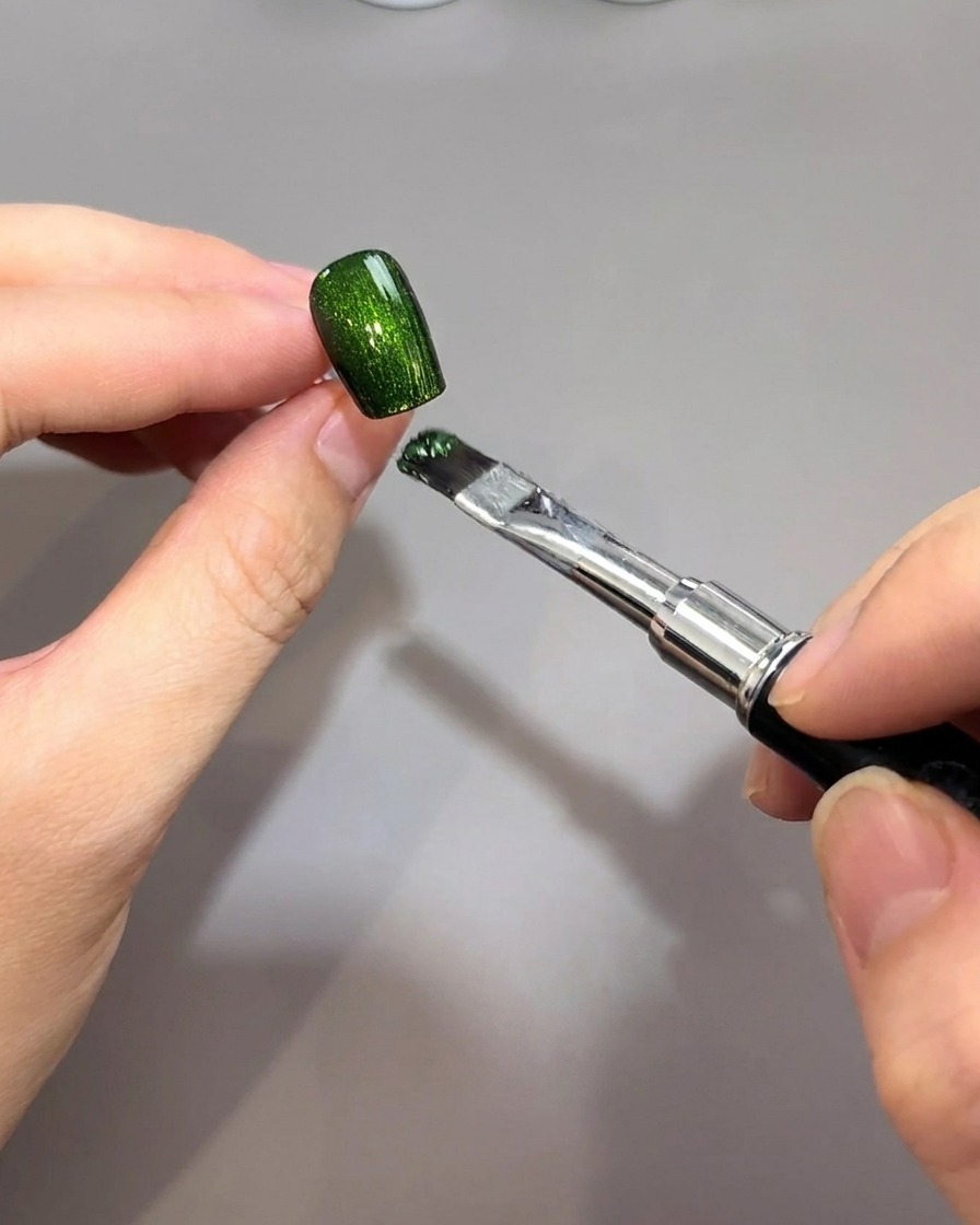 Ein Pinsel trägt ein leuchtend smaragdgrünes, magnetisches Gel auf eine schwarze Nagelbasis auf.