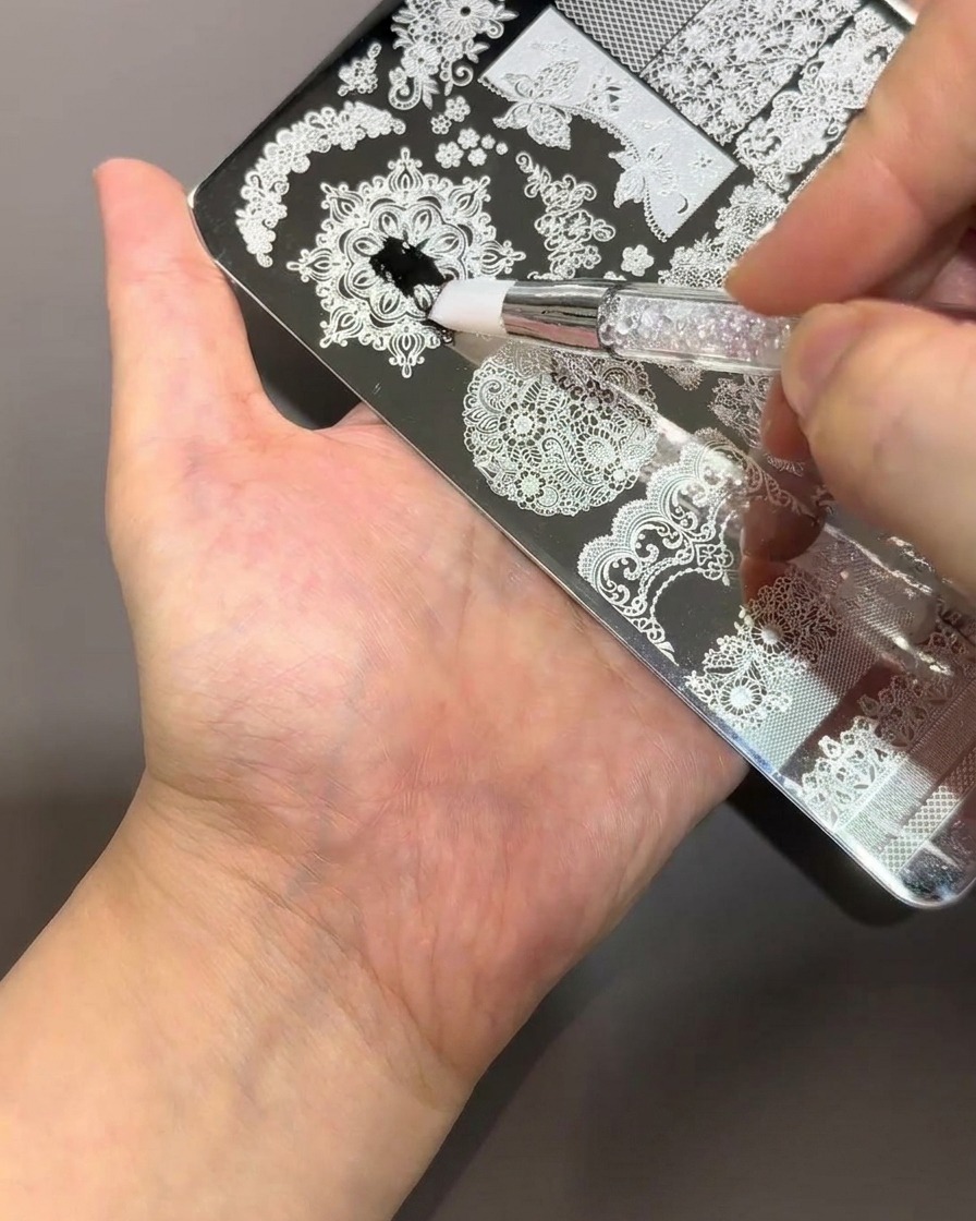 Ein Pinsel trägt dicken schwarzen Lack auf eine silberne Metall-Stamping-Platte mit komplizierten Spitzen- und Blumenmustern auf.