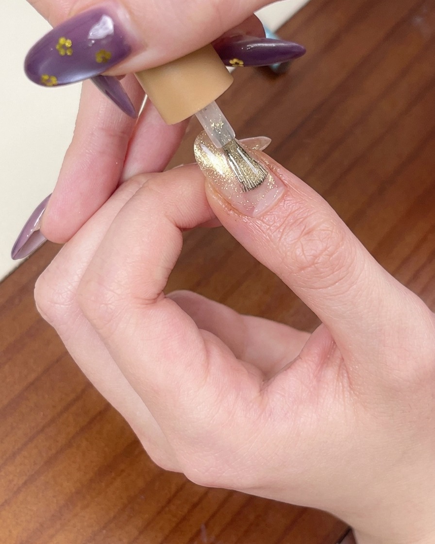 Ein Pinsel trägt eine Schicht schimmerndes roségoldenes Cat-Eye-Gel auf den Nagel auf.