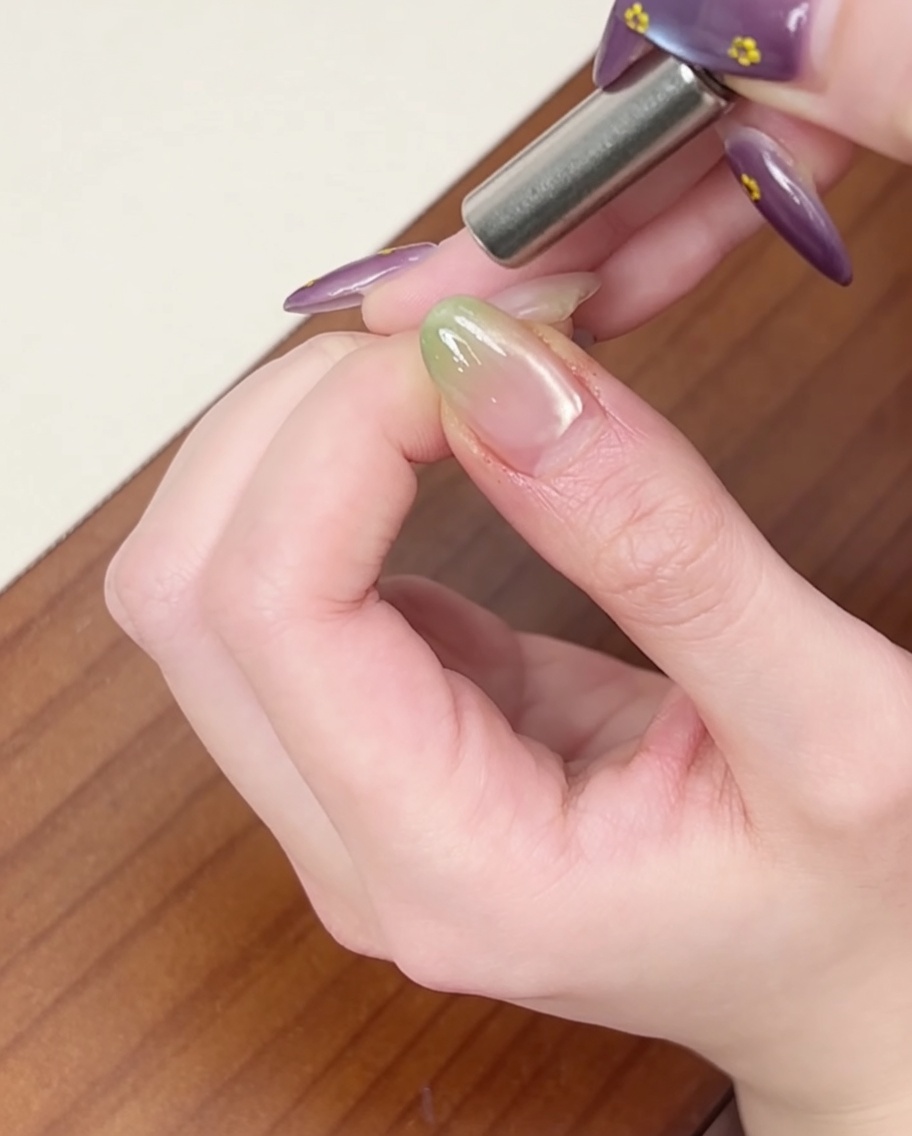 Ein zylindrischer Magnet wird seitlich an den Nagel gehalten, um einen Cat-Eye-Schimmereffekt zu erzeugen.