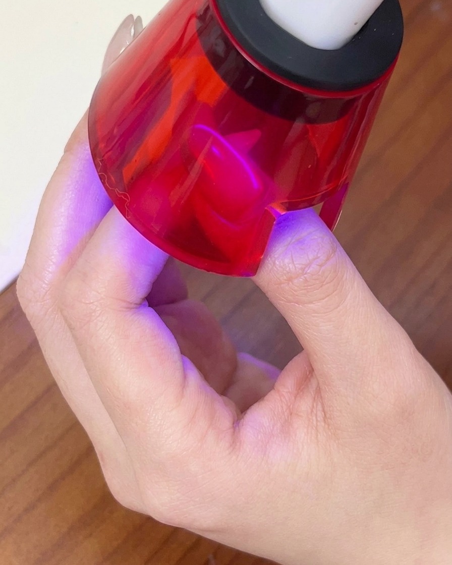 Ein Finger härtet unter einer roten Hand-LED-Lampe aus, um das magnetische Gel-Design zu fixieren.