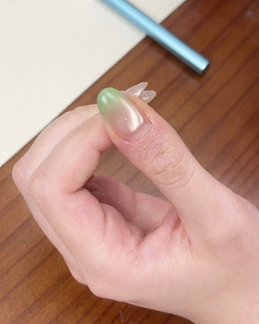 Ein Fingernagel mit einer grünen Verlauf-Spitze unter einer tragbaren roten Mini-UV-Lampe.