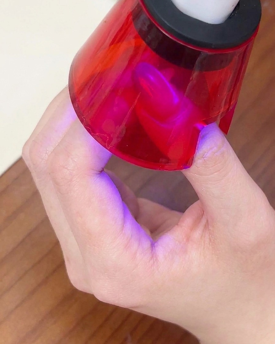 Ein fertiger Nagel härtet unter einer kleinen roten tragbaren UV-Lampe aus.