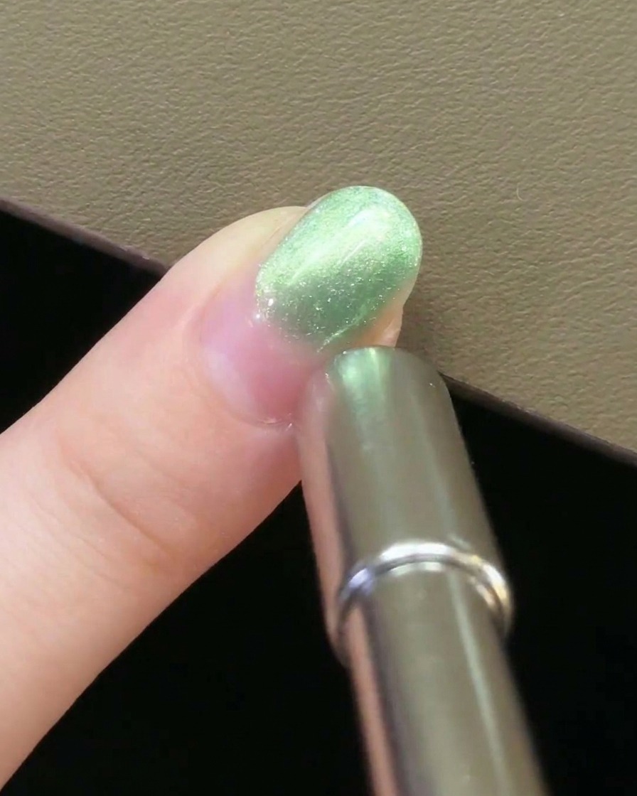 Ein Nagelmagnet aus Metall wird parallel zur Seite eines mit grünem Magnetgel lackierten Fingernagels gehalten.