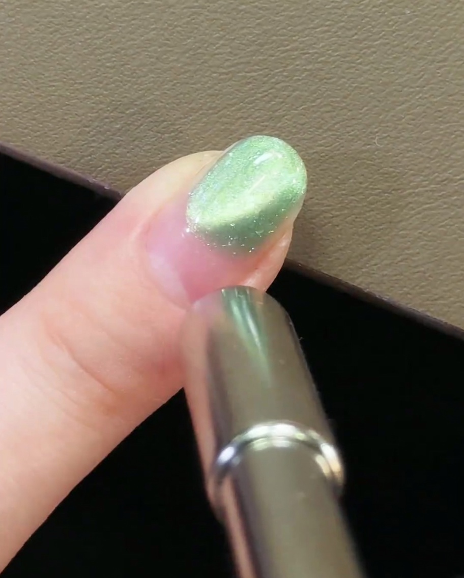Ein Nagelmagnet am hinteren Nagelrand eines mit grünem Cat-Eye-Gel lackierten Nagels.