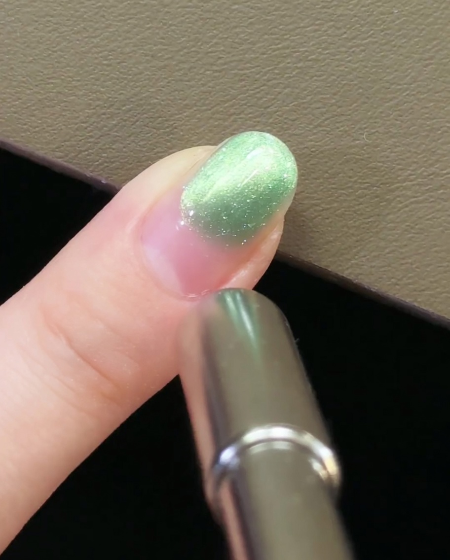 Eine Hand zieht ein magnetisches Werkzeug vom Fingernagel weg, um das Cat-Eye-Muster zu sichern.
