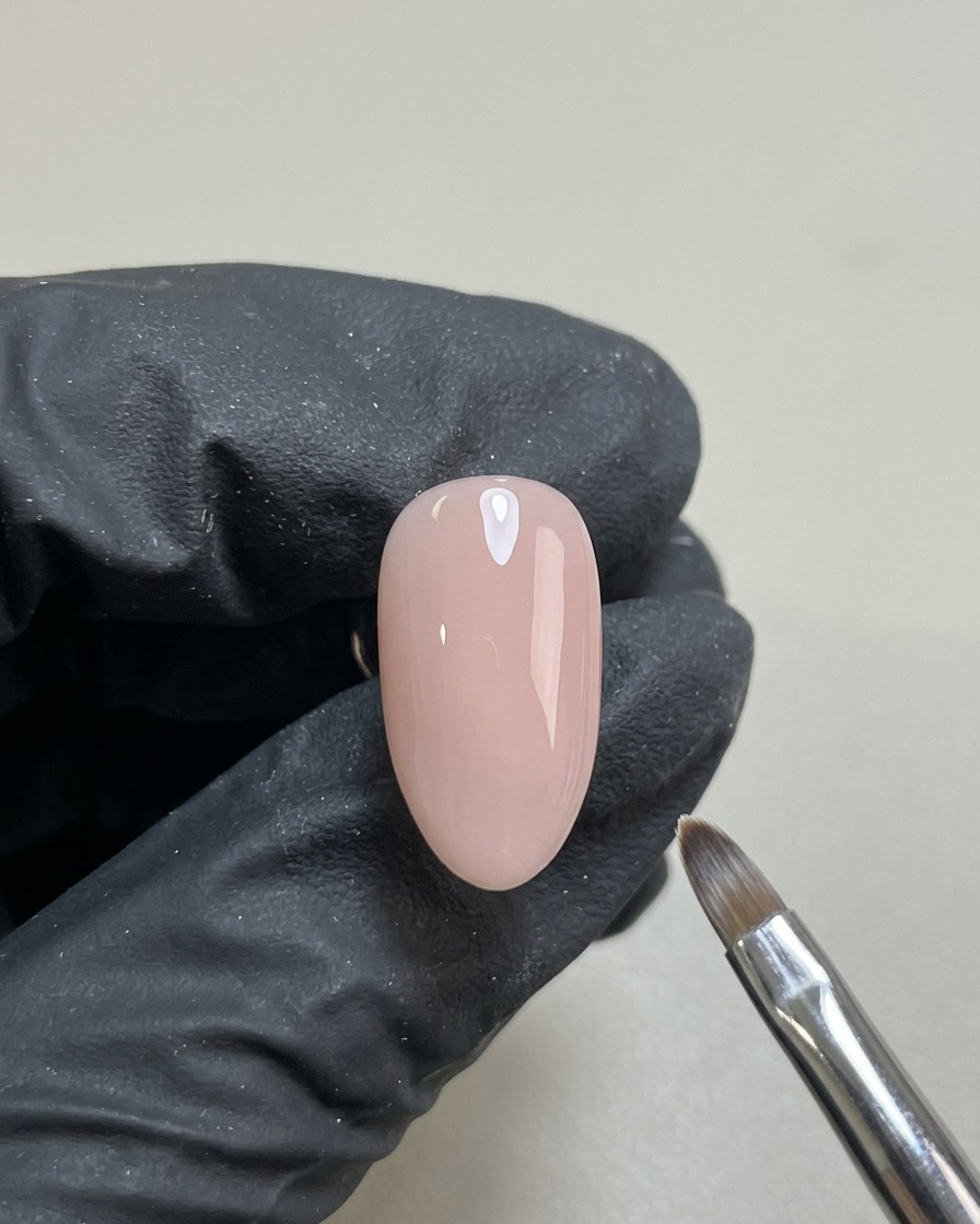 Ein Nagel mit einer gleichmäßigen, halbtransparenten Nude-Gelschicht, ausgehärtet und bereit für das Design.