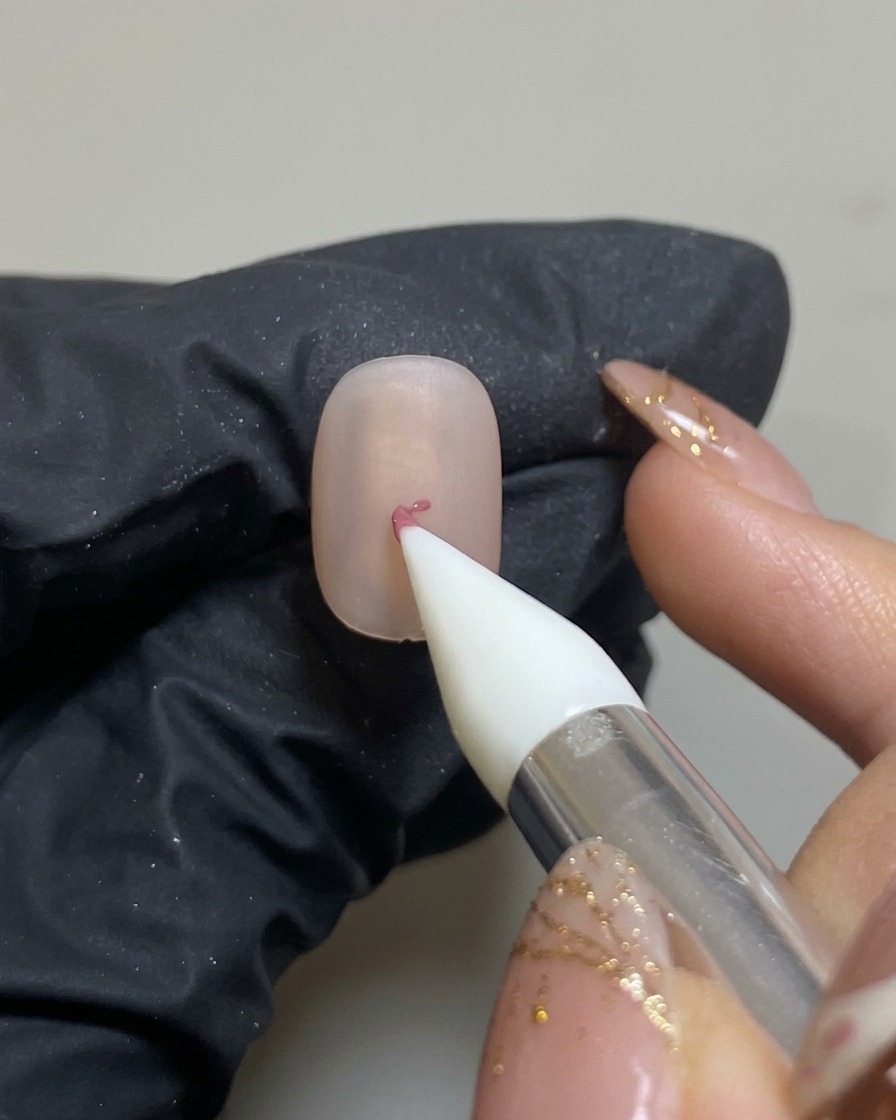 Ein Silikon-Nageltool platziert einen kleinen Punkt rosa Gel in der Mitte des matten Nagels.