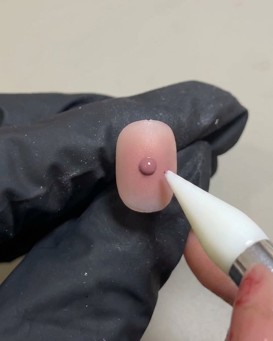 Ein Silikon-Tool trägt einen kleinen, konzentrierten Punkt rosa Gel auf den bereits ausgehärteten Verlauf auf.