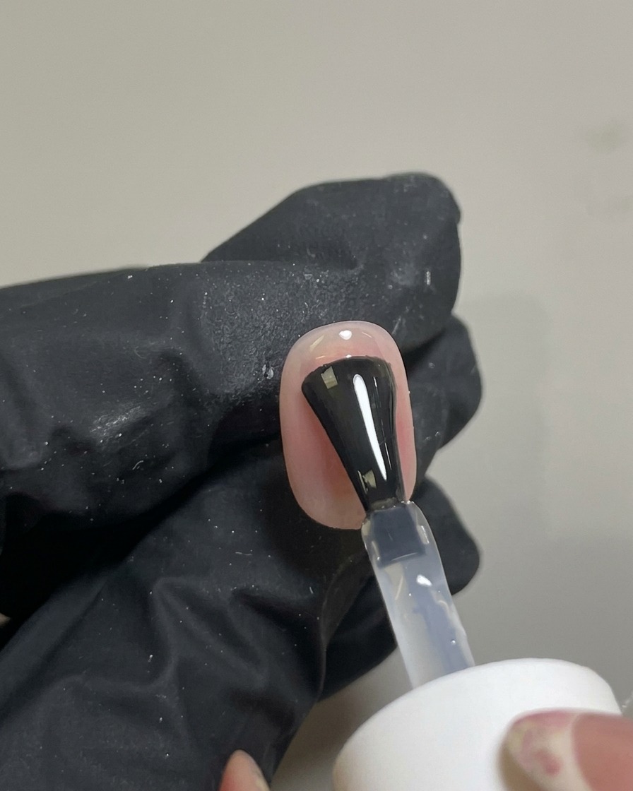 Ein Pinsel trägt einen klaren Hochglanz-Top-Coat über das fertige Nageldesign auf.