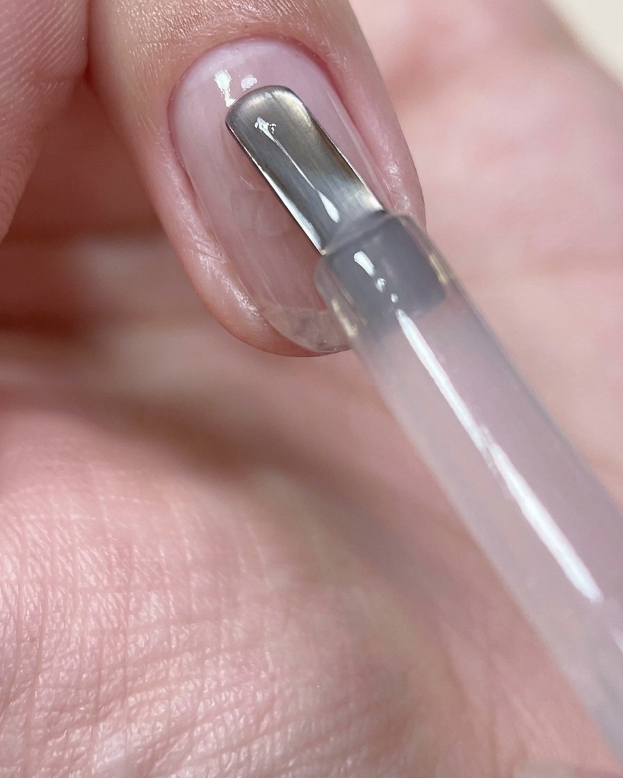 Ein Nagelpinsel, der einen Tropfen zartrosa Aufbaugel in der Mitte eines vorbereiteten Naturnagels platziert.