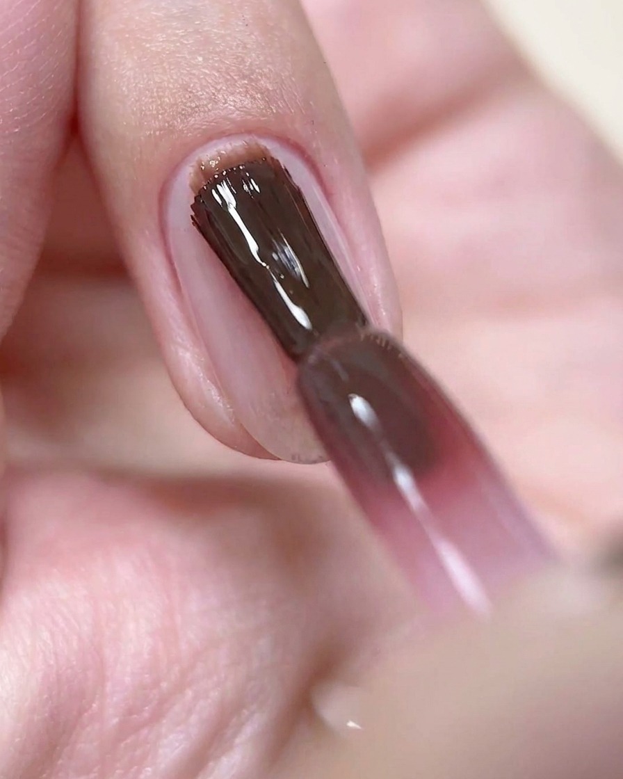 Ein Nagelpinsel trägt eine dünne Schicht weinrosa Gel-Lack auf einen vorbereiteten Nagel auf.