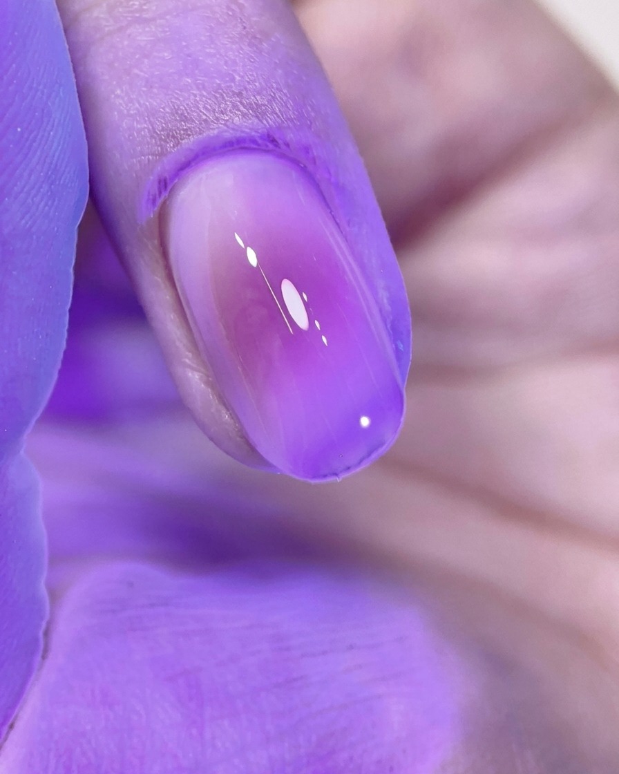 Ein wunderschön manikürter, rosa Blush-Nagel, der unter dem hellen violetten Licht einer UV/LED-Nagellampe aushärtet.