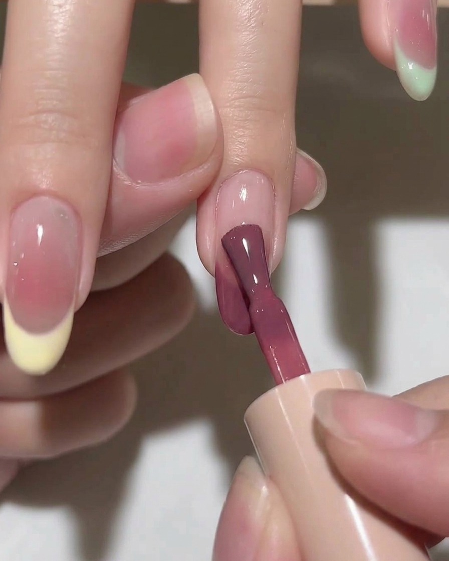 Ein Pinsel verblendet einen Tropfen rosa Gel auf dem Nagel und kreiert einen weichen, kreisförmigen Farbverlauf.
