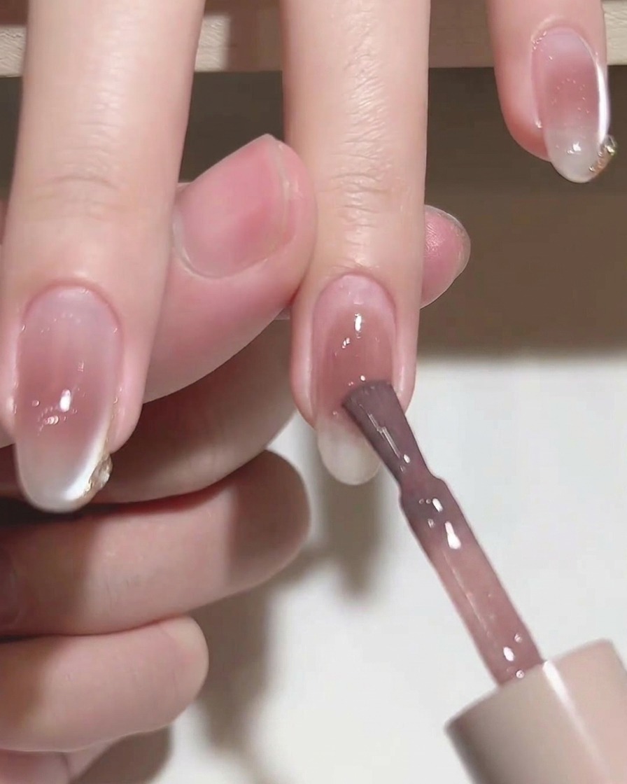 Ein flacher Gelpinsel glättet rosa Gellack auf einem Nagel.