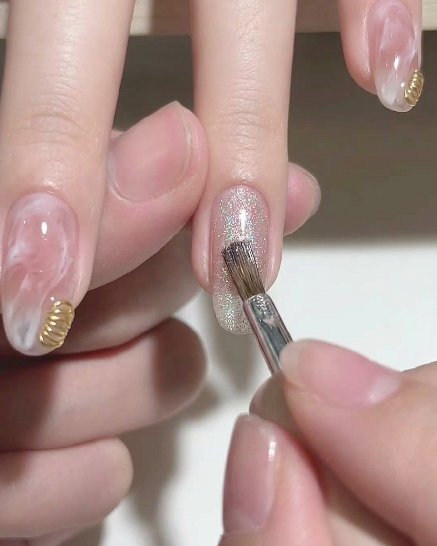Ein Pinsel trägt silbernes, glitzerndes Cat-Eye-Gellack auf die Spitze eines rosa Gelnagels auf.