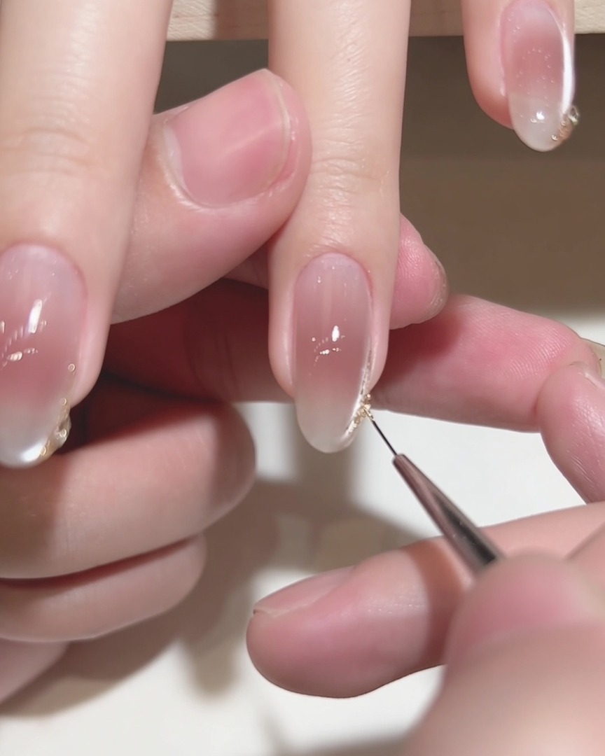 Nahaufnahme eines feinen Liner-Pinsels beim Auftragen von Golddetails auf eine Nagelspitze.