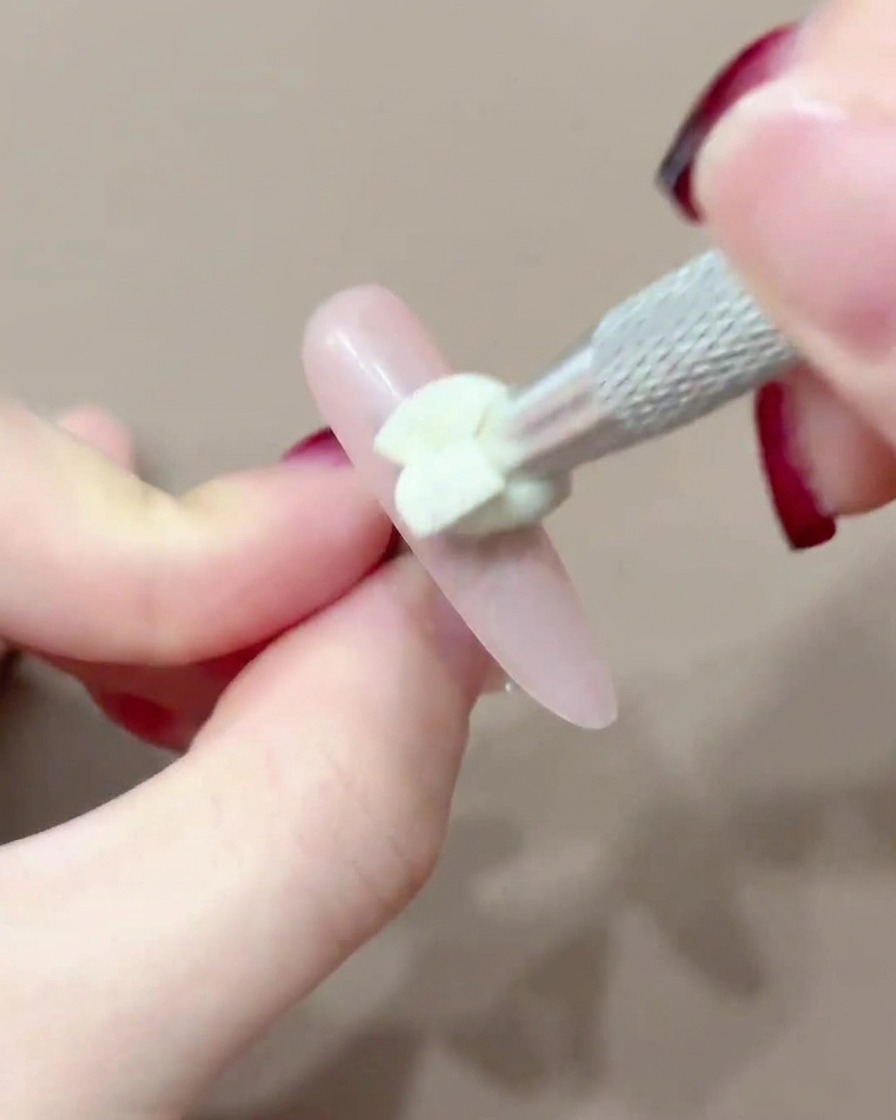 Ein Silikon-Applikator tupft rosa Pigment auf die Mitte eines Nagels.