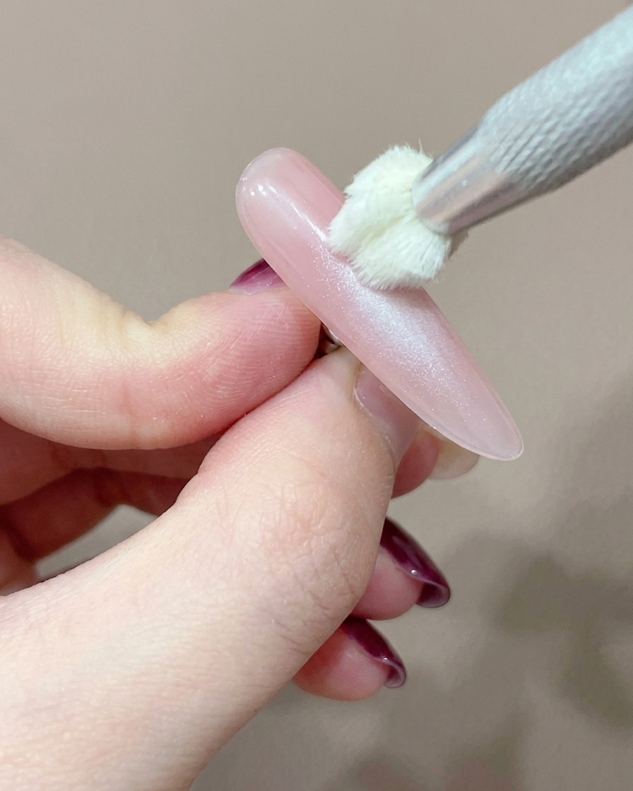 Ein Silikon-Applikator fügt vorsichtig einen konzentrierten Punkt rosa Gel in die Mitte des Nagels hinzu.