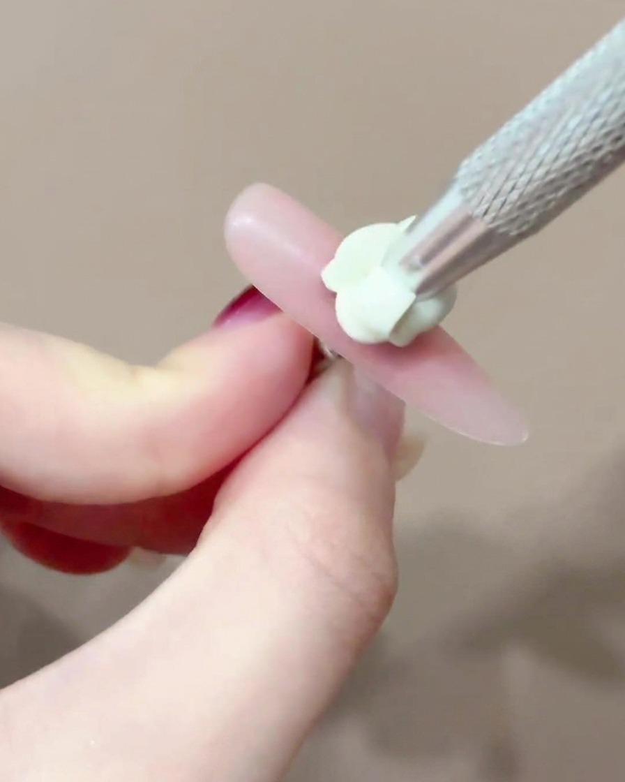Ein Pinsel trägt einen kleinen, präzisen Punkt rosa Blush-Gel auf die Mitte eines Nagels auf.